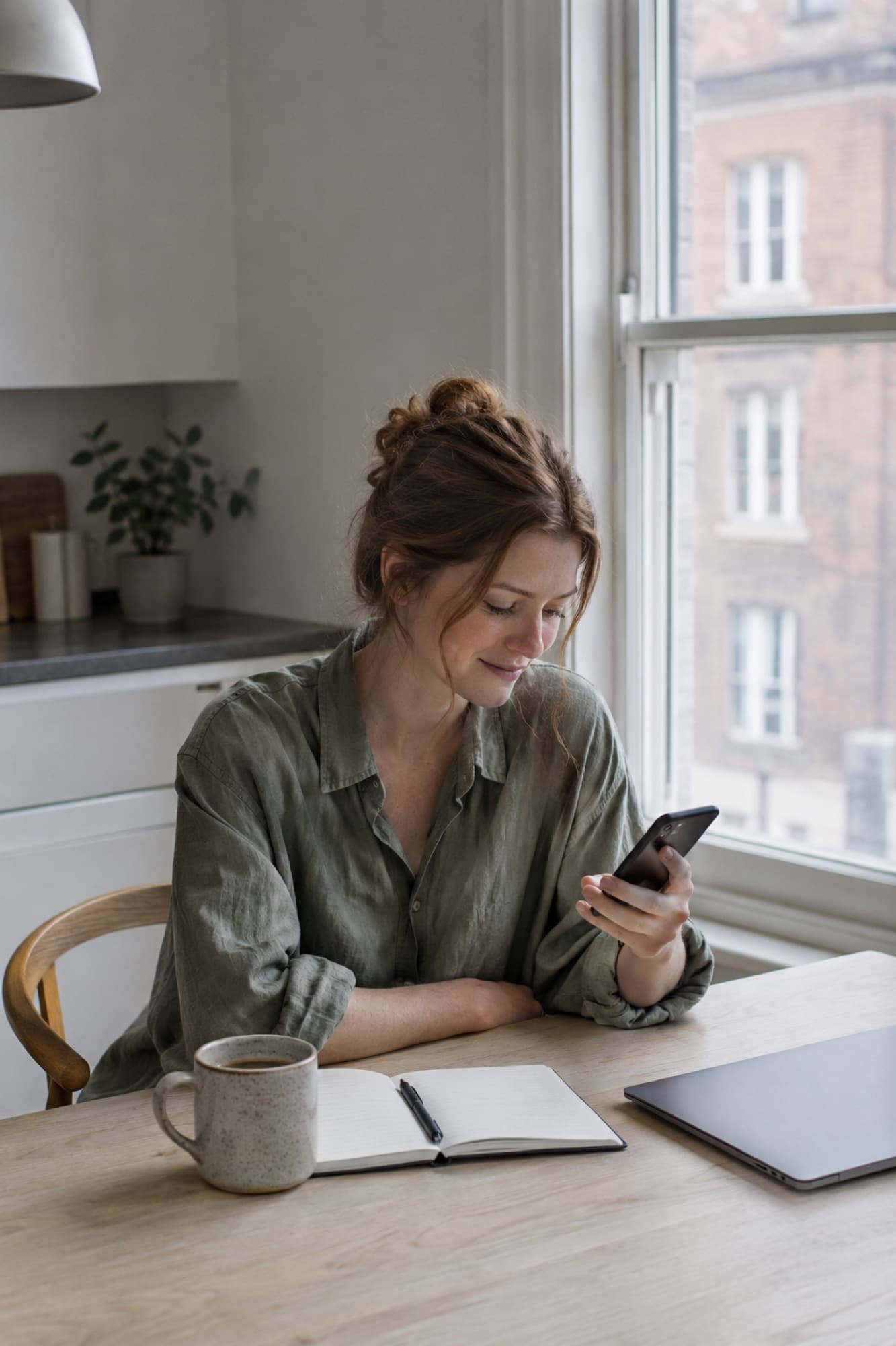 A freelancer at her kitchen table glancing at her phone over morning coffee